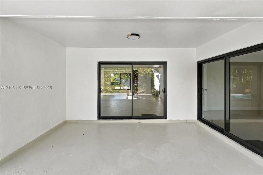 Covered patio featuring concrete flooring, neutral wall finishes, flush-mount ceiling lighting, and black-framed sliding glass doors