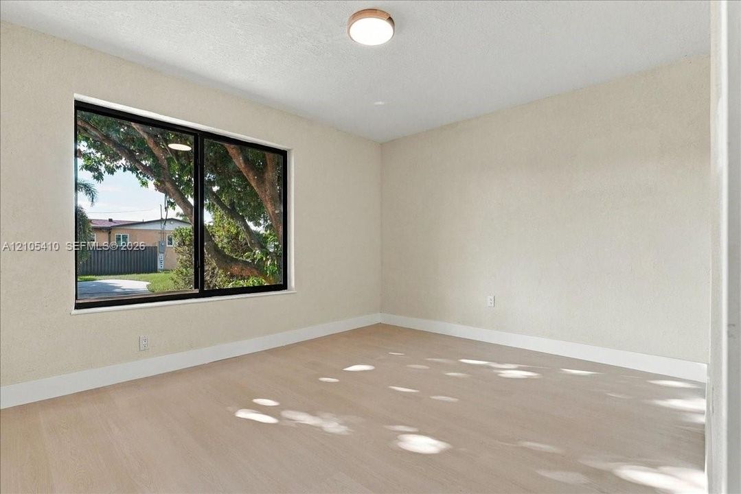 Neutral-toned interior featuring wood-finish flooring, a large picture window with dark framing, and a flush-mount ceiling light fixture