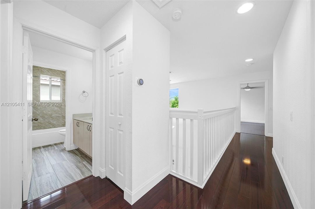 Hallway featuring dark wood-finish flooring, white baluster railing, and recessed lighting