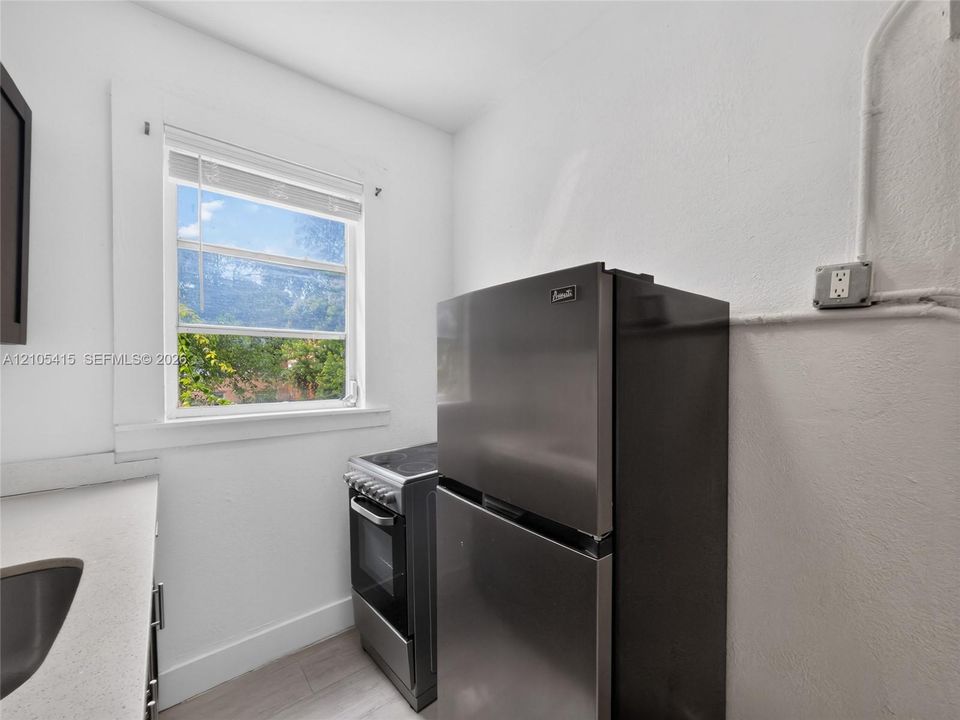 Stainless steel refrigerator and freestanding range, neutral solid-surface countertop, and window with natural illumination
