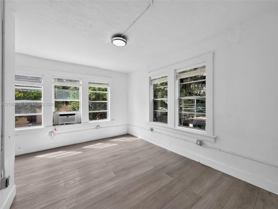 Bright corner room featuring expansive multi-pane windows flooding the space with natural light, wood-finish flooring, clean white walls, and recessed ceiling lighting
