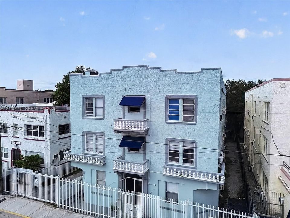 Three-story stucco exterior featuring a stepped parapet roofline, multiple cantilevered balconies with decorative balustrades, and fixed fabric awnings
