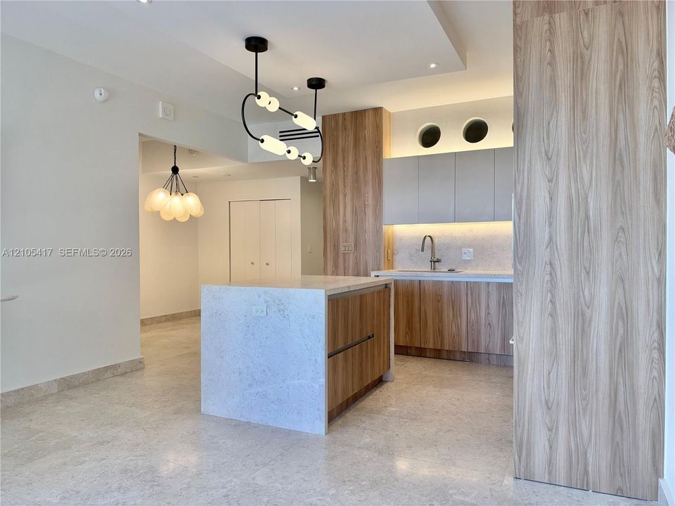 Kitchen featuring a central island with a stone countertop, wood-finish cabinetry, under-cabinet lighting, and a stainless steel sink with a gooseneck faucet