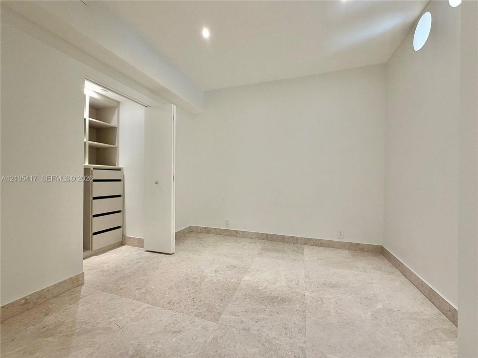 Recessed lighting, three circular wall cutouts, light-toned stone tile flooring, and a cased doorway