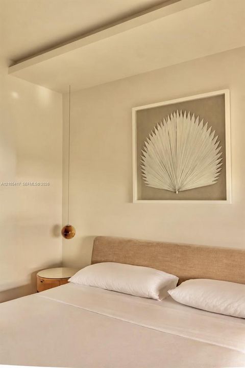 Recessed ceiling panel, fabric upholstered headboard, suspended spherical light fixture, and wood-finish side table with white top