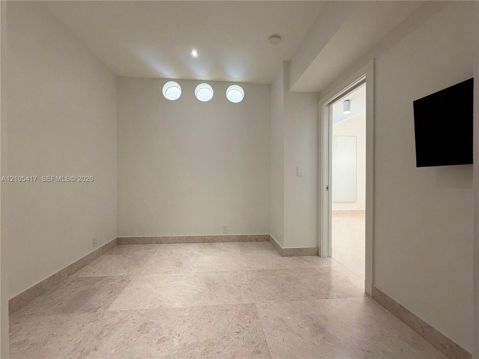 Recessed ceiling lighting, three flush-mount wall sconces, neutral wall paint, and stone tile flooring