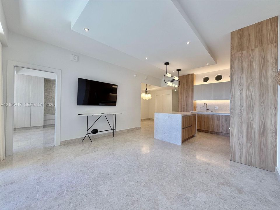Recessed lighting, wood-finish cabinetry, a central kitchen island, light-toned tile flooring, and a contemporary pendant light fixture