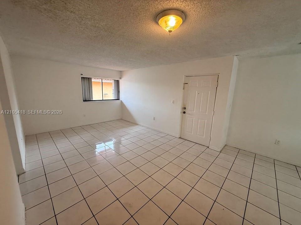 Spacious room featuring white tile flooring, a window with horizontal blinds, and a paneled entry door
