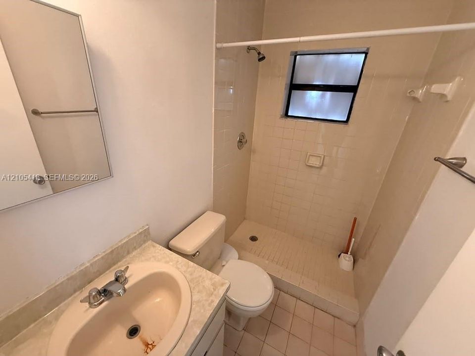 Bathroom featuring a vanity with an integrated sink, a wall-mounted mirror, a tiled shower enclosure, and a window