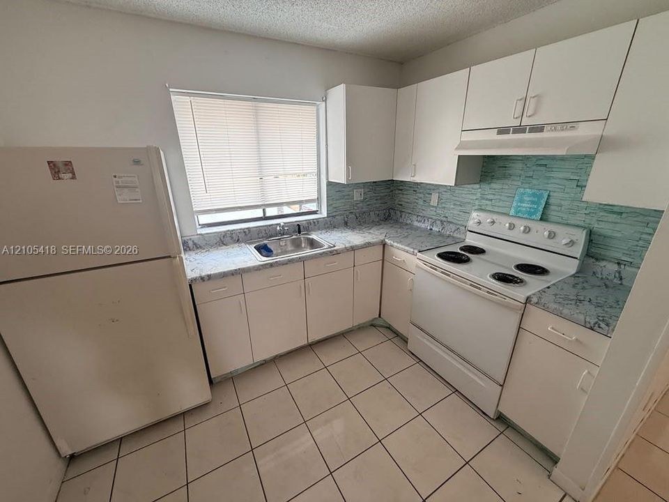 White cabinetry with chrome hardware, coordinating white appliances, a stainless steel sink, and light-toned tile flooring