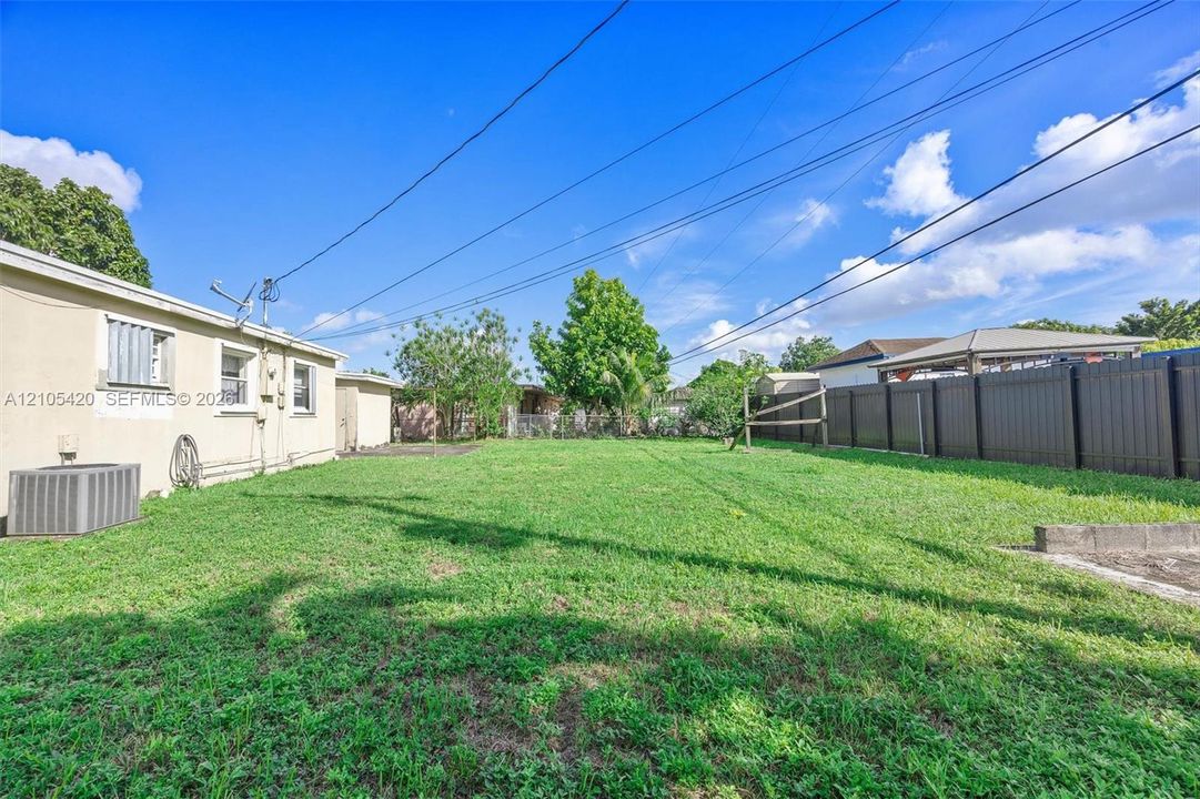 Expansive grass yard with a dark privacy fence and concrete slab