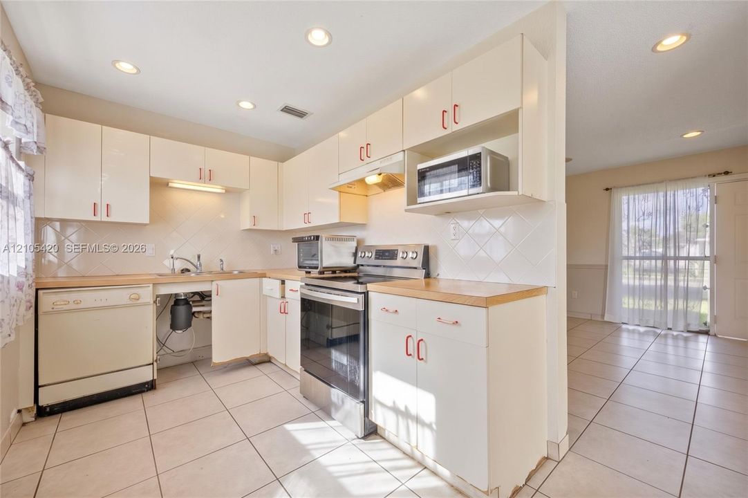 Kitchen featuring white cabinetry with red hardware, light wood-finish countertops, and a white tile backsplash