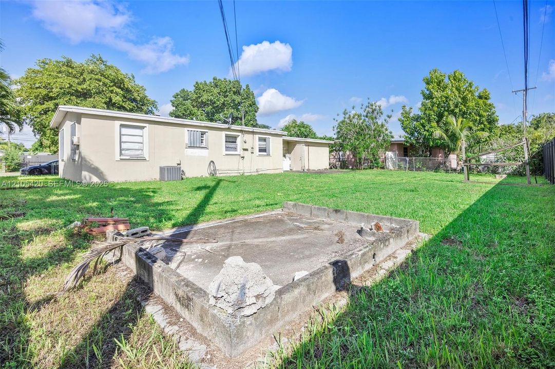 Expansive backyard with a concrete pad and chain-link fencing, featuring a single-story residence with multiple windows and an exterior AC unit