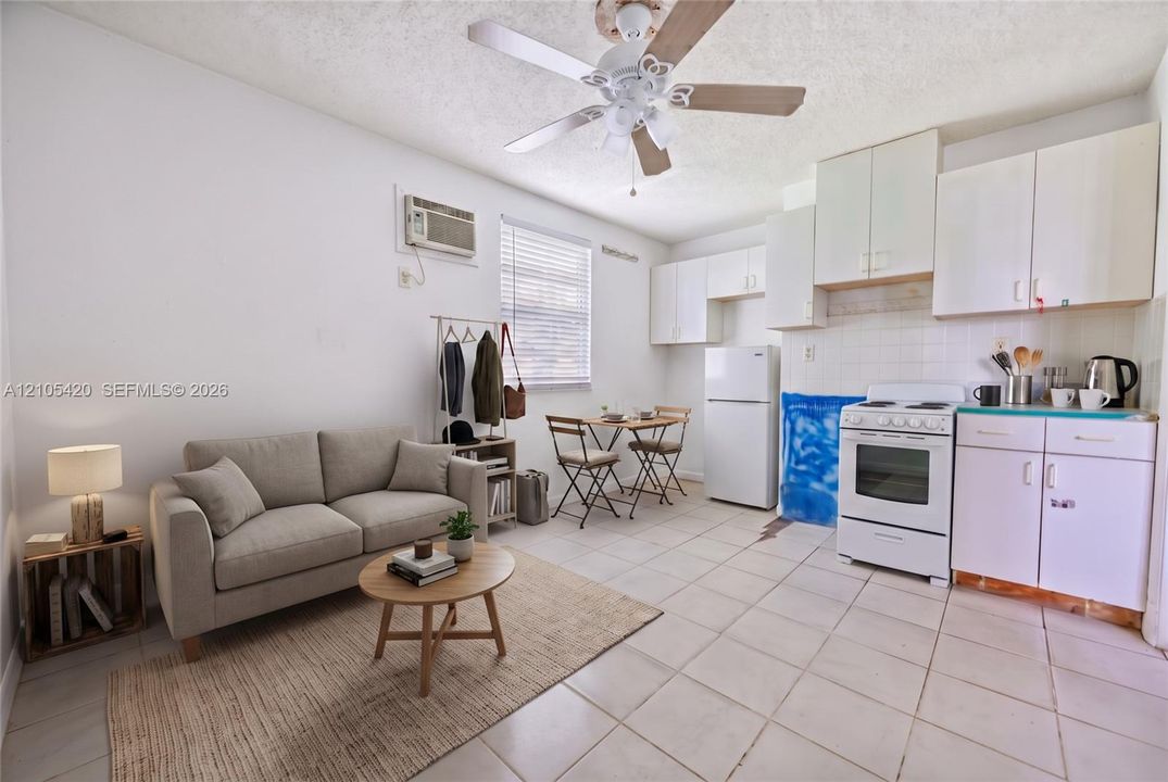 White kitchen cabinetry with a tile backsplash, ceiling fan, and window with blinds