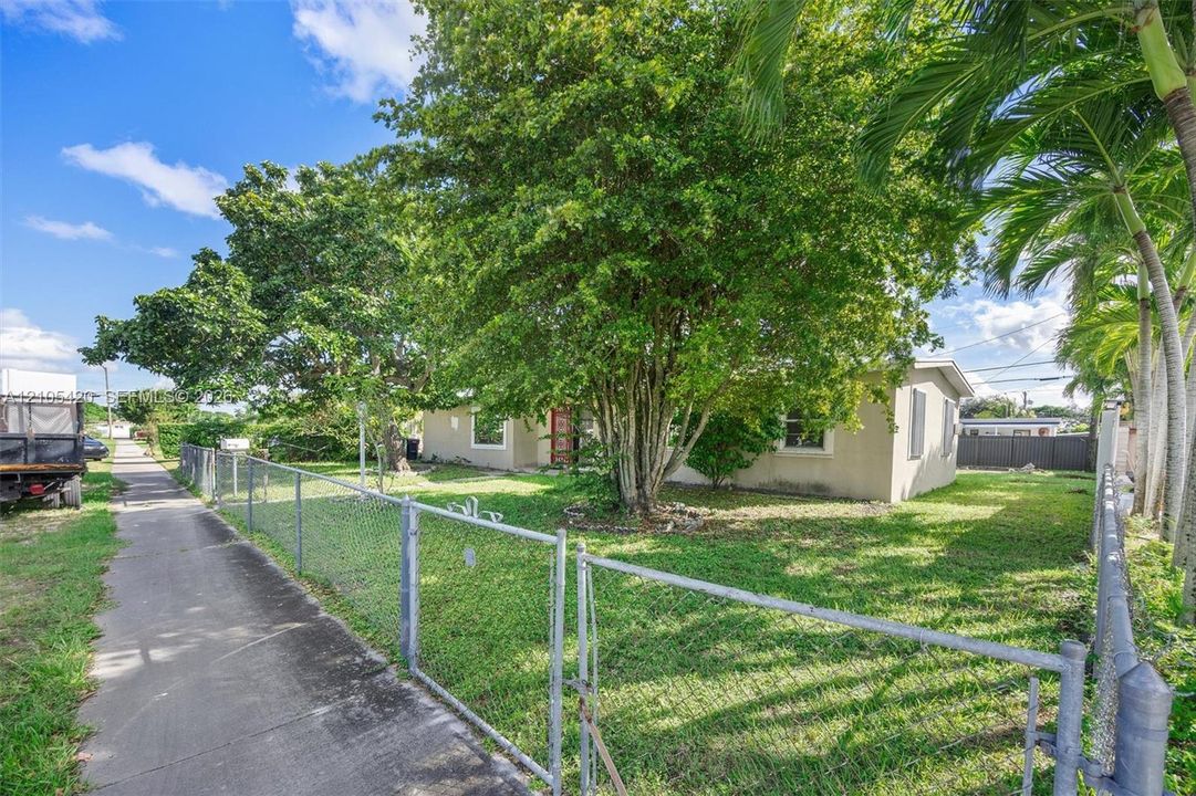 Fenced property with a manicured lawn, established landscaping, and mature palm trees