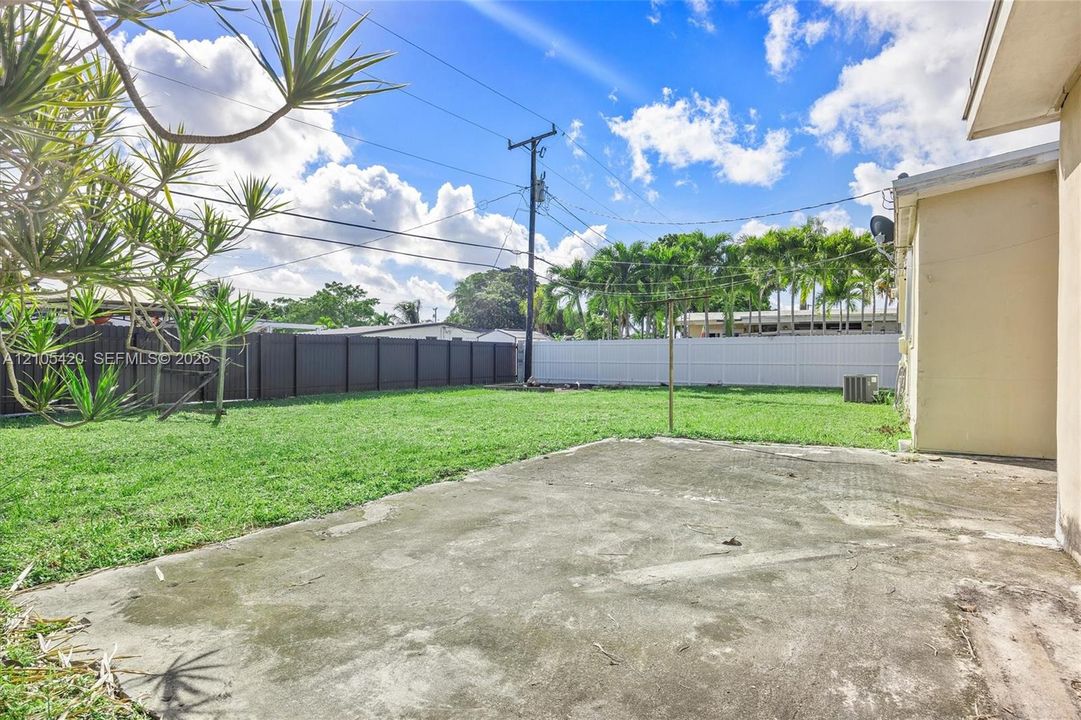 Expansive concrete patio with a large grassy area, surrounded by a dark privacy fence and a white privacy fence