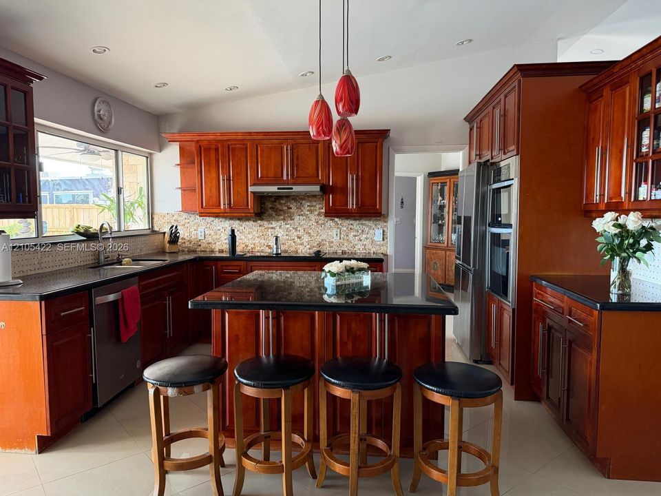 Kitchen featuring cherry-toned cabinetry, dark stone countertops, a multi-tiered glass pendant lighting fixture, a decorative mosaic tile backsplash, and a central island with integrated storage