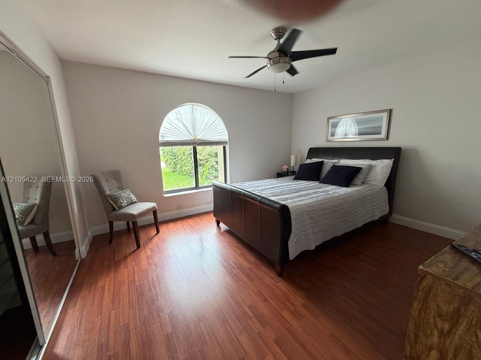Arched window with decorative fanlight, wood-finish flooring, full-height mirrored sliding closet doors, and ceiling fan with integrated light fixture