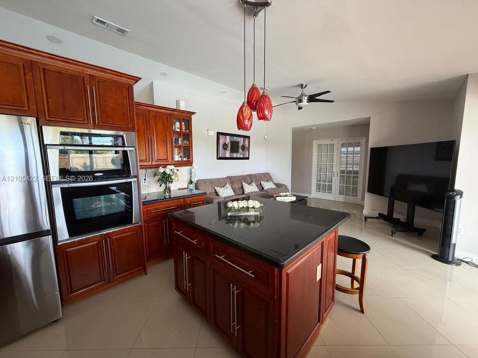 Kitchen featuring wooden cabinetry, central island with stone countertop, stainless steel double wall oven, and three-pendant lighting