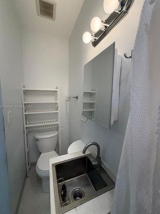 Stainless steel drop-in sink with a high-arch faucet, stone-composite countertop, wall-mounted medicine cabinet, and three-bulb vanity light fixture