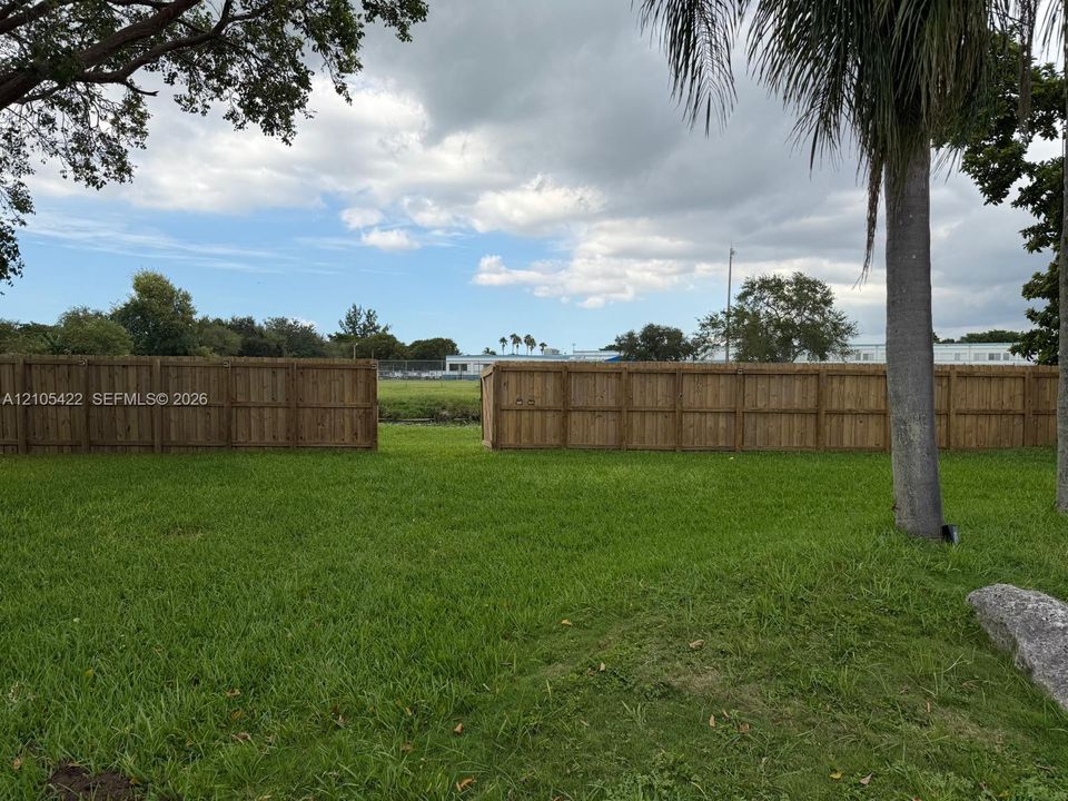Expansive backyard featuring a grass lawn, mature trees, and a wooden privacy fence