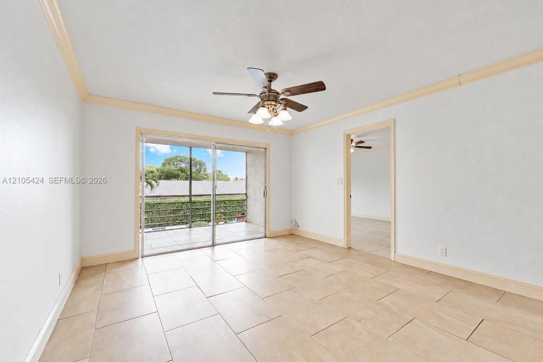 Sliding glass door to balcony, tile flooring, ceiling fan, crown molding, and doorway to additional space