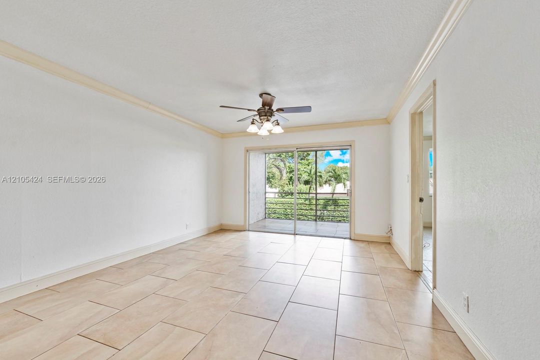 Large format tile flooring, crown molding, ceiling fan with light kit, sliding glass door access to balcony, and a doorway with trim