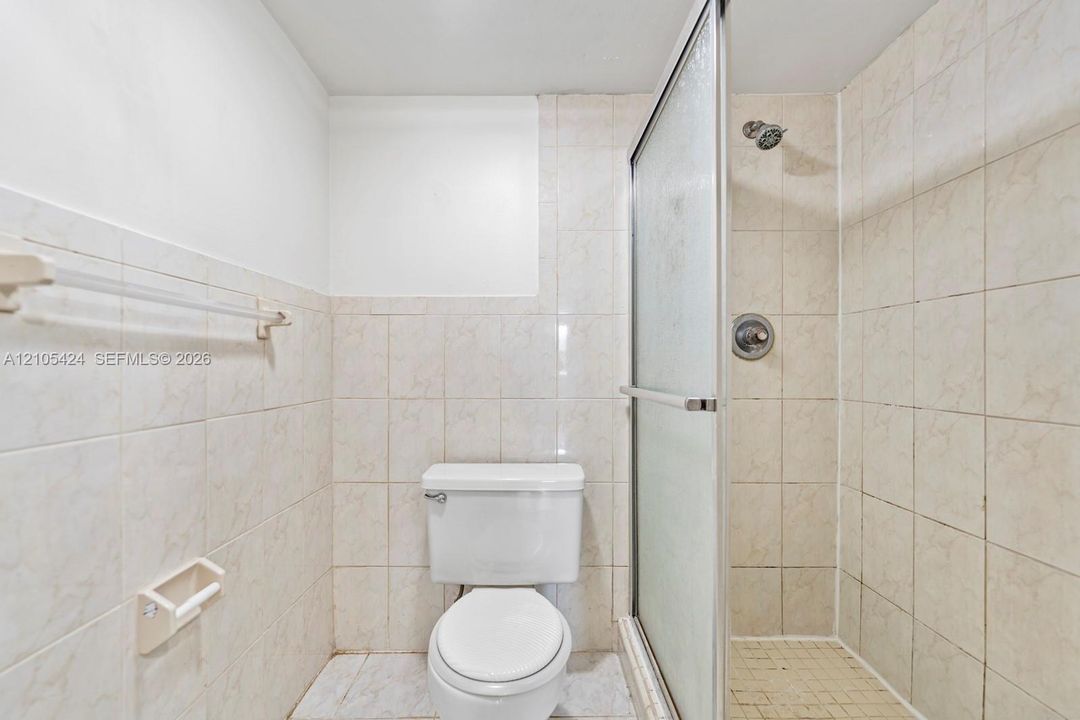 Tiled bathroom featuring a white toilet and a shower with a frosted glass enclosure
