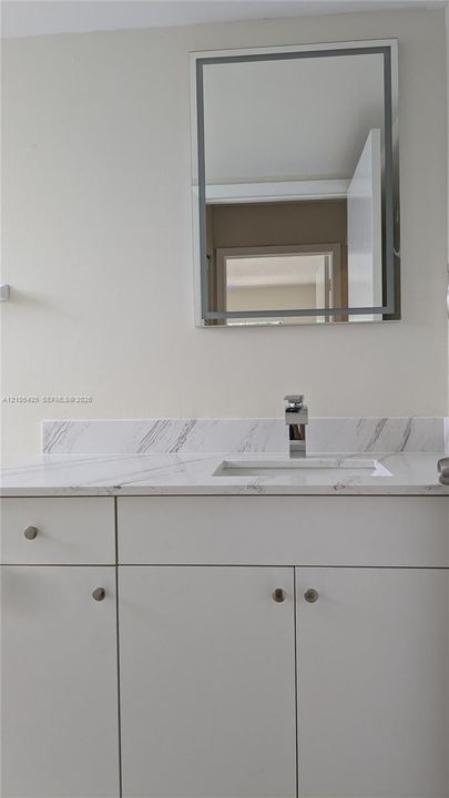 White floating vanity with a polished chrome faucet, rectangular undermount sink, and a framed wall mirror