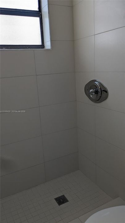 White tiled shower enclosure with a chrome shower control and a small window