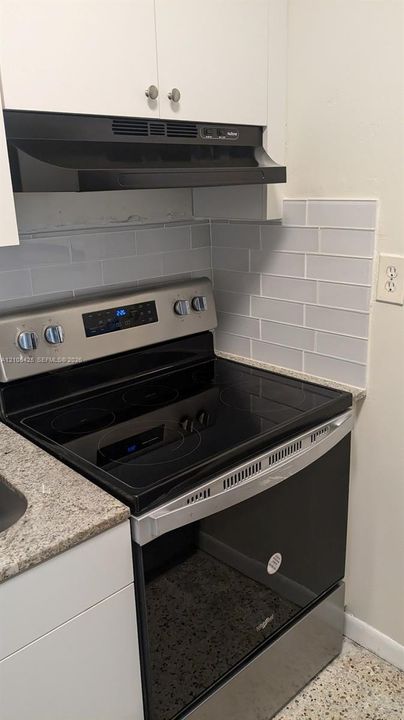 Stainless steel electric range with a smooth cooktop, complemented by light grey subway tile backsplash and a speckled countertop