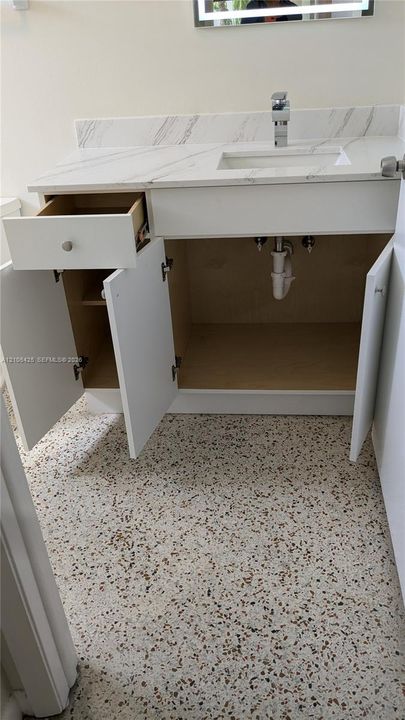 White vanity with an integrated sink, polished chrome faucet, and a light-toned countertop with veining