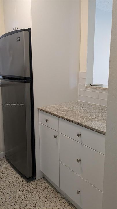 Stainless steel refrigerator, white cabinetry, integrated drawer storage, stone-finish countertop, and subway tile backsplash