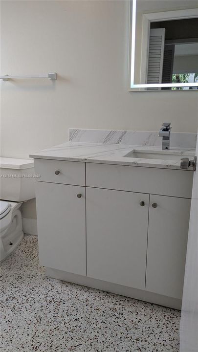 White vanity with a light-toned countertop, integrated sink, and a framed mirror with integrated lighting