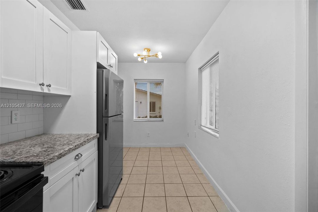 White shaker cabinetry, subway tile backsplash, stainless steel refrigerator, granite-style countertops, and tile flooring