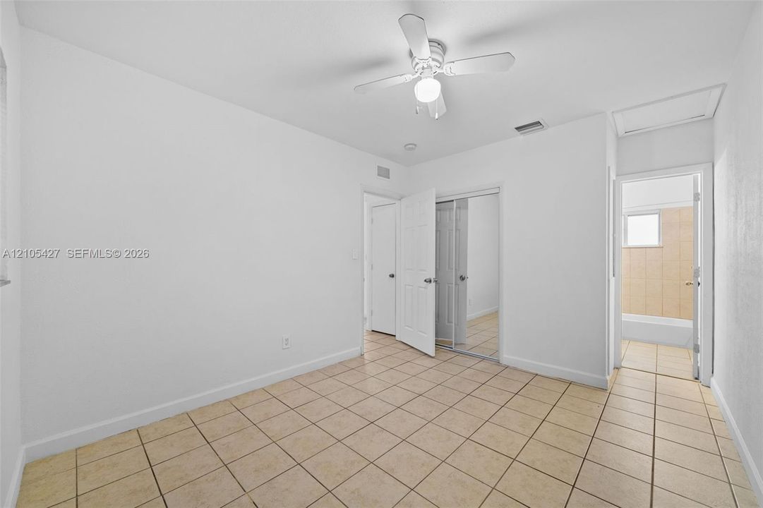 Neutral-toned tile flooring, ceiling fan with light fixture, and white painted walls