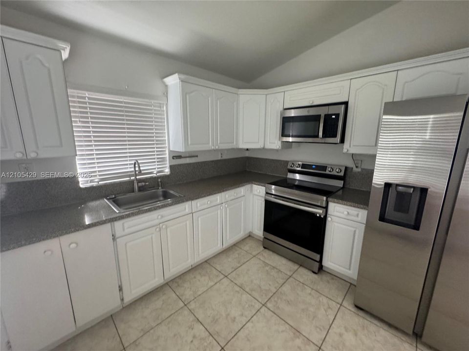 White cabinetry with decorative molding, stainless steel appliances, speckled countertops, tile flooring, and a stainless steel sink with a high-arc faucet