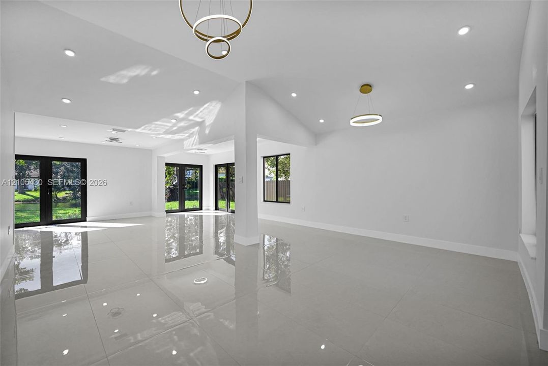 Large-format porcelain tile flooring, vaulted ceilings, recessed lighting, double-ring modern pendant fixtures, and black-framed French doors