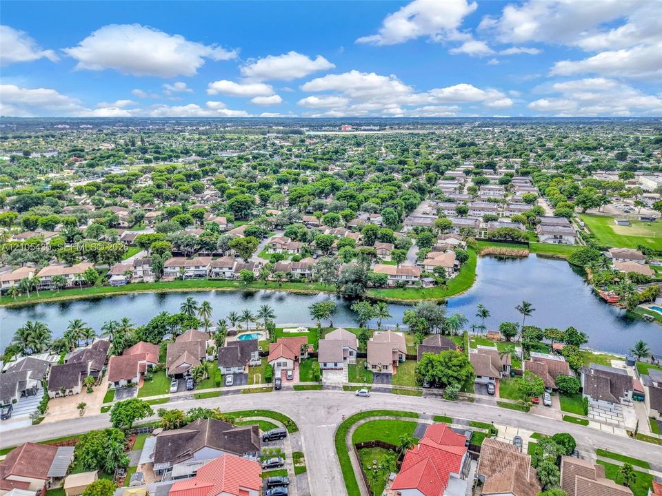 Aerial perspective of a residential community featuring a sprawling lake, mature trees, paved roadways, and varied roofline architecture