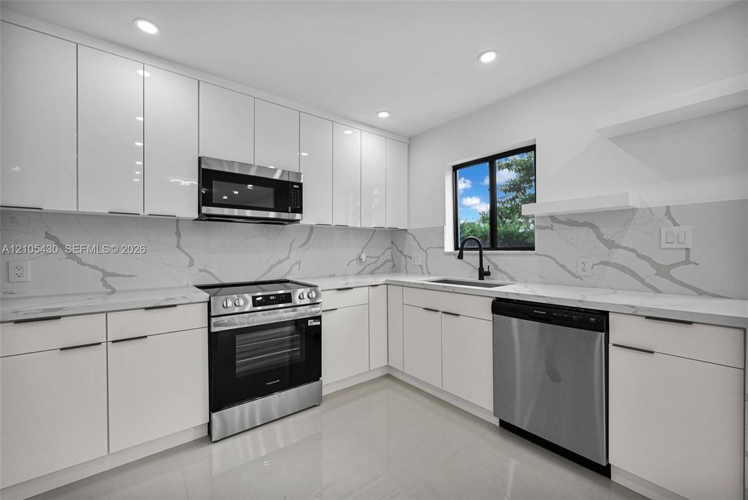 Contemporary kitchen featuring sleek white cabinetry, stone-finish countertops, full-height decorative backsplash, stainless steel appliances, and recessed lighting