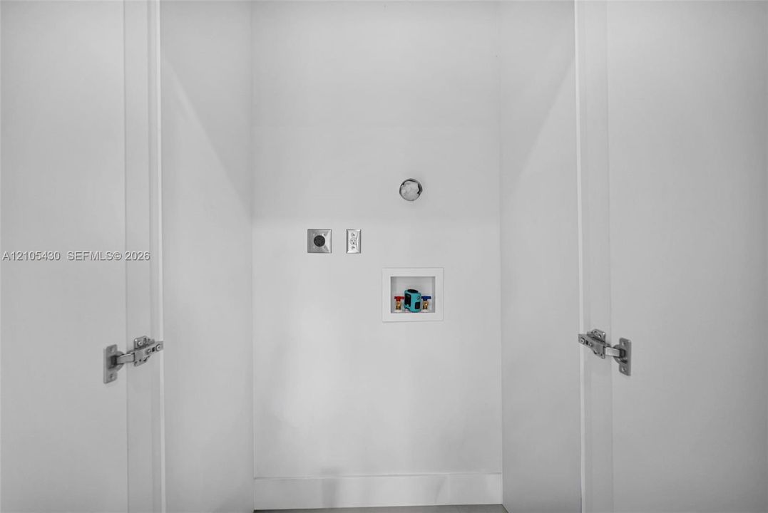Dedicated laundry alcove featuring double swing doors, recessed plumbing hookups, and integrated electrical outlets