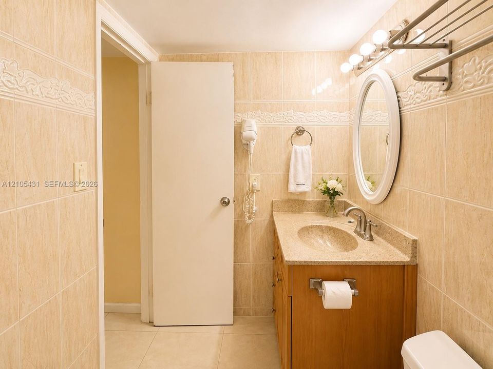 Tiled bathroom featuring a wood-finish vanity with an integrated sink, an oval wall-mounted mirror, and a five-bulb vanity light fixture