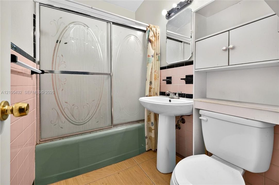 Bathroom featuring a pedestal sink, built-in cabinetry, tiled wall surround, and a tub-shower combination with etched glass sliding doors