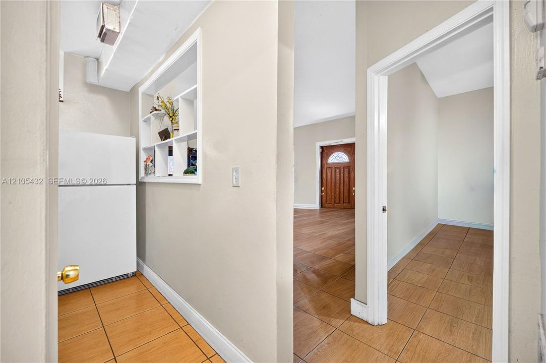 Interior space featuring neutral wall paint, wood-finish tile flooring, built-in wall shelving, and a solid wood entry door with glass pane detail