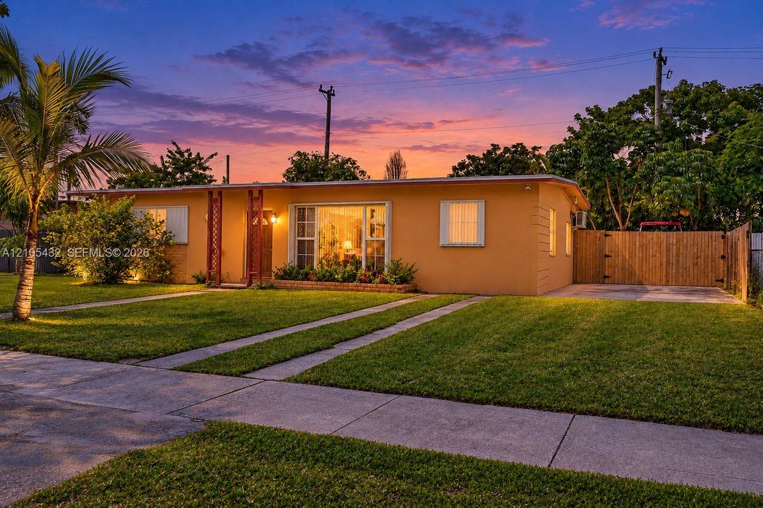 Single-story residence featuring a stucco exterior, expansive front lawn, paved dual-strip driveway, and a wooden privacy fence