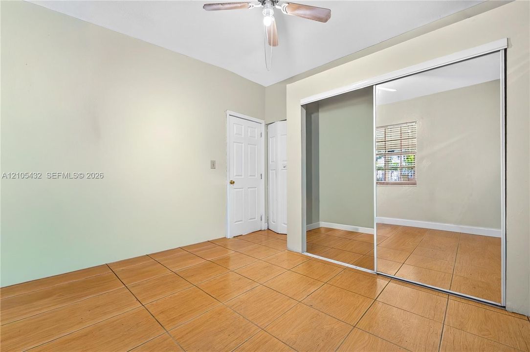 Interior room featuring wood-finish tile flooring, ceiling fan with light fixture, mirrored sliding closet doors, and multi-panel interior door