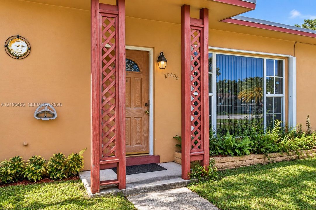 Exterior facade featuring custom lattice-work support columns, an arched-glass pane entry door, a multi-pane picture window, and a stone-lined planter bed