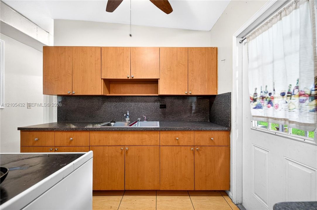 Natural wood-finish cabinetry, dark countertop with integrated dual-basin sink, and tile flooring