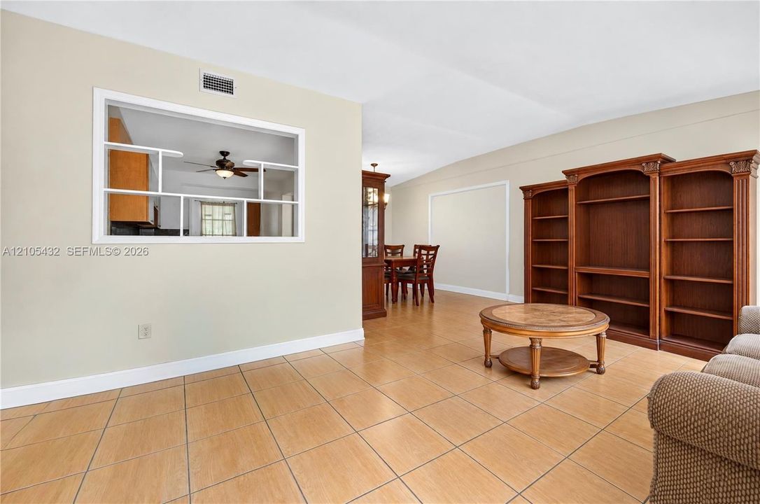 Open-concept interior featuring large-format tile flooring, built-in floor-to-ceiling wooden shelving, and a decorative pass-through window with paneled detailing