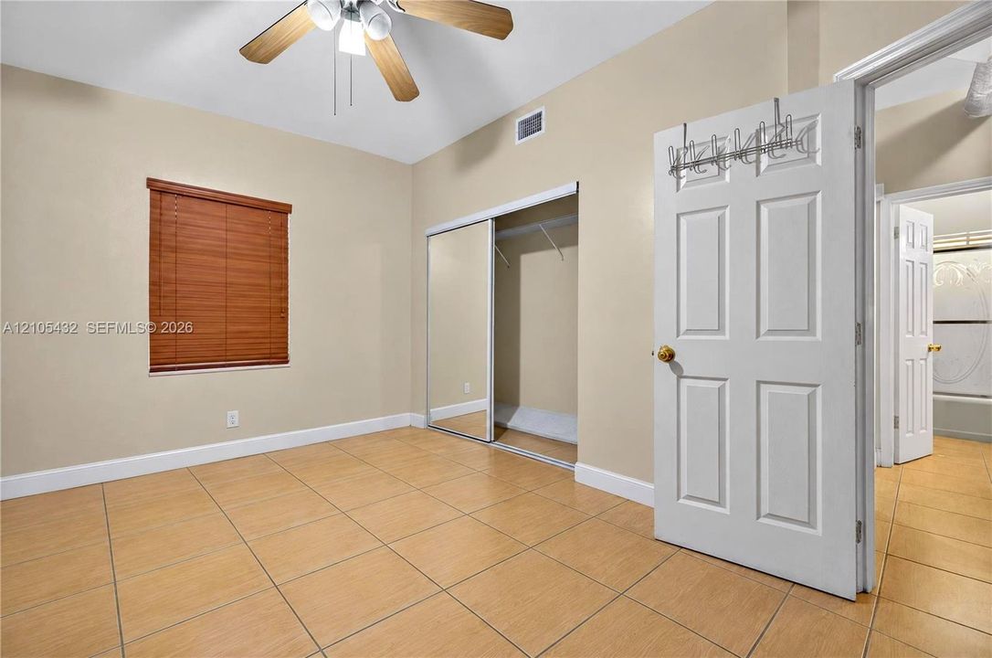 Ceramic tile flooring, ceiling fan with integrated lighting, closet with mirrored sliding doors, and horizontal slat window blinds